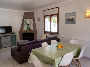 A living room with a fireplace, a television, a sofa, a dining table with chairs, and a painting on the wall. - House mit private pool in L'Escala-HUTG-006380 (l'Escala)