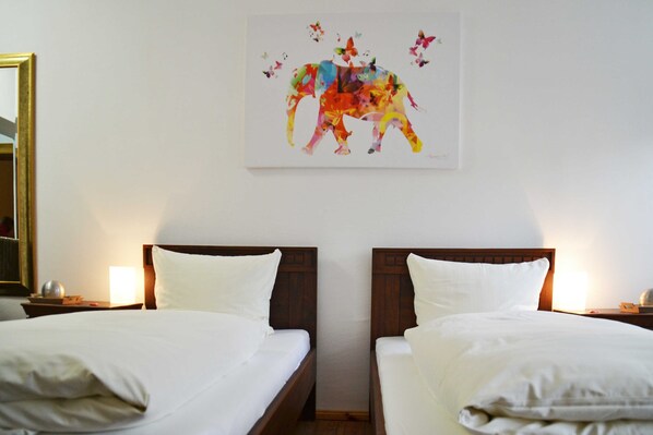 A hotel room with two beds, a large mirror, and a colorful artwork on the wall.
