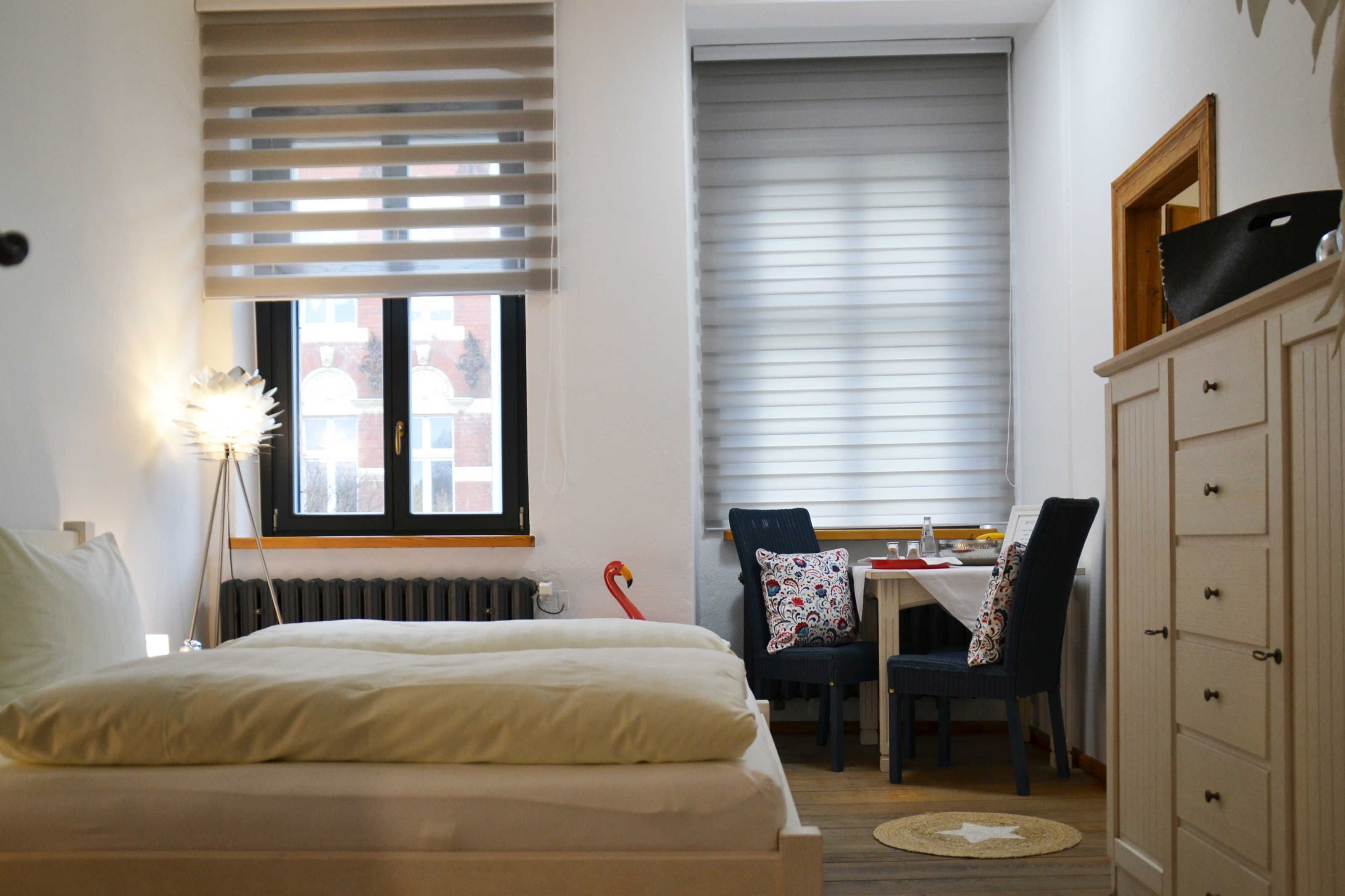 Een slaapkamer met een bed, een bureau met stoelen, een radiator en een kledingkast.