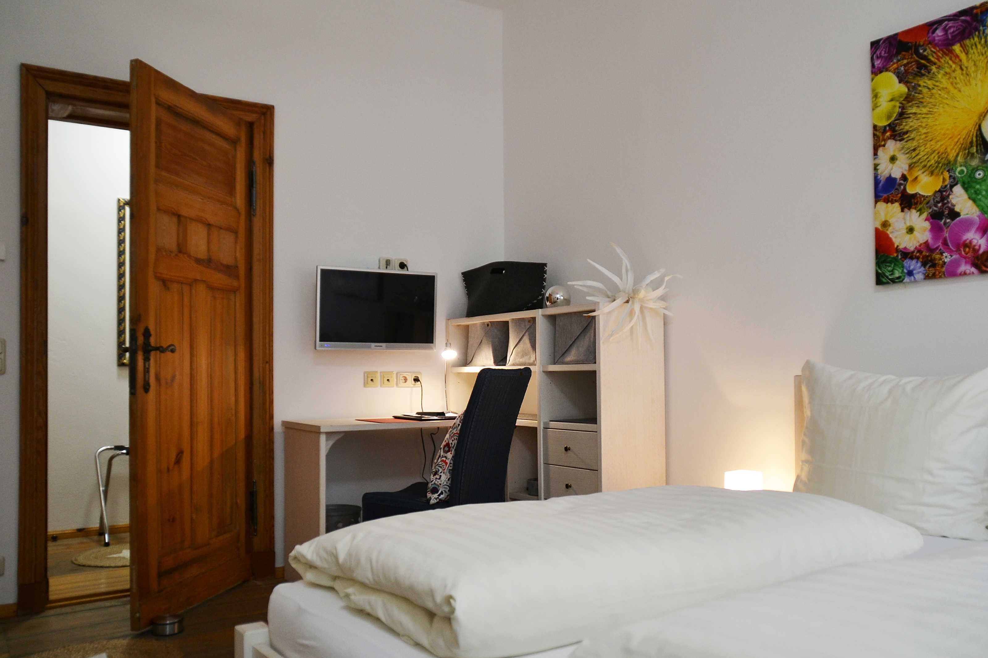 Een slaapkamer met een bed, een bureau met een computer, een stoel, een televisie en een deur.