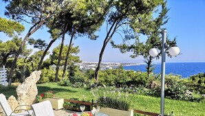 An outdoor seating area with a table set for two, surrounded by chairs, overlooking a coastal landscape with trees and a view of the sea. - Louis Luxury Villa (Rhodes)