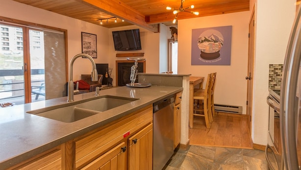 A kitchen with a double sink, wooden cabinets, a built-in dishwasher, and a dining area with a table and chairs. - Easy Mountain - Mt Crested Butte (Crested Butte)