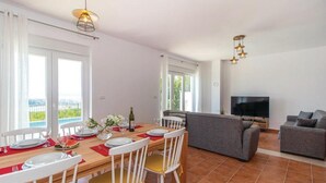 A dining area with a table set for four, a sofa, a TV, and a balcony view. - Holiday Home-big Swimming Pool-amazing Views (Kraljevica)