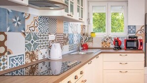 A kitchen with patterned tiles, a coffee maker, a microwave, and a window with a view of greenery. - Holiday Home-big Swimming Pool-amazing Views (Kraljevica)