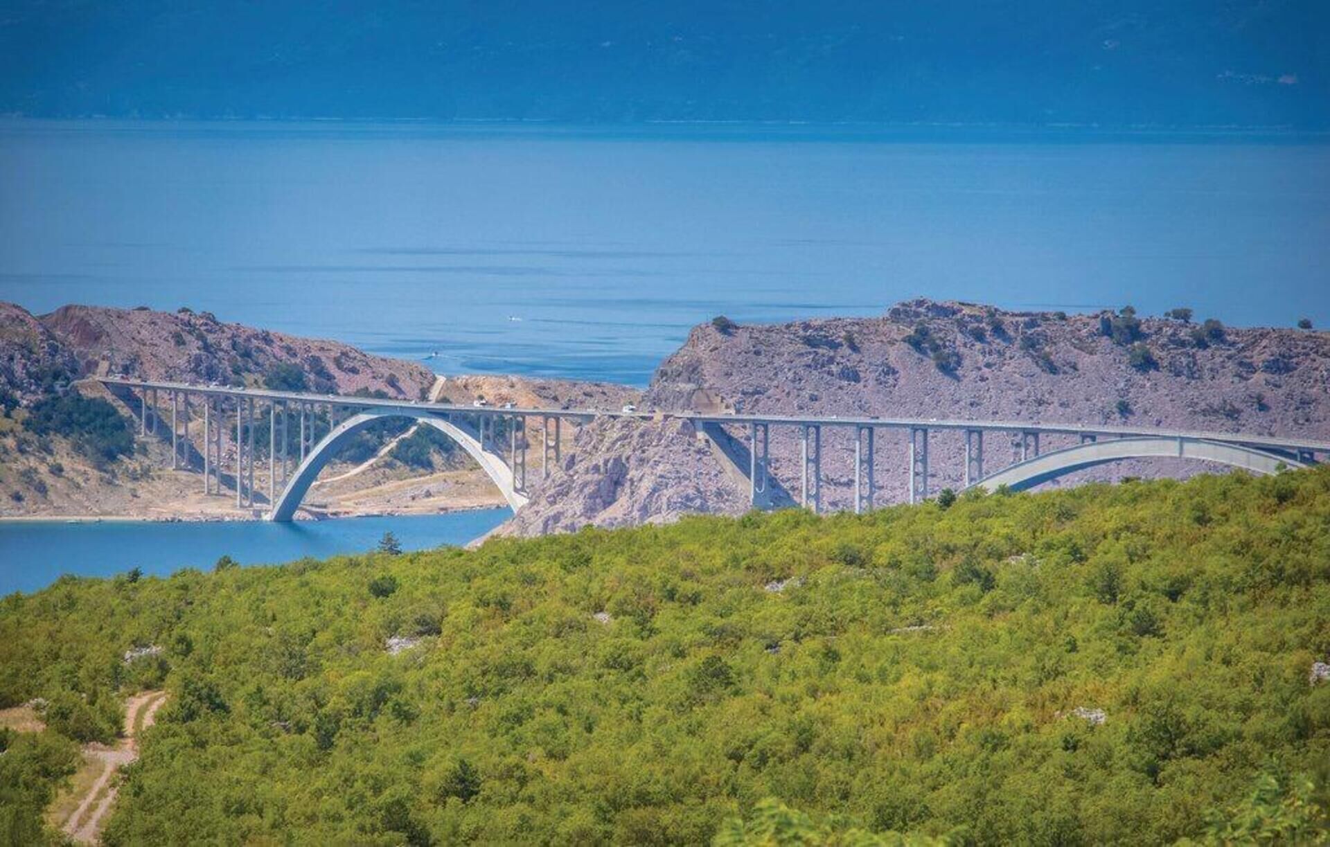 Un pont enjambant une étendue d’eau, avec un terrain rocheux et une végétation luxuriante au premier plan.