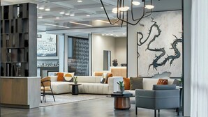A modern interior with a sectional sofa, a grey armchair, a coffee table, and a bookshelf. - AC Hotel by Marriott Austin Hill Country (Austin)