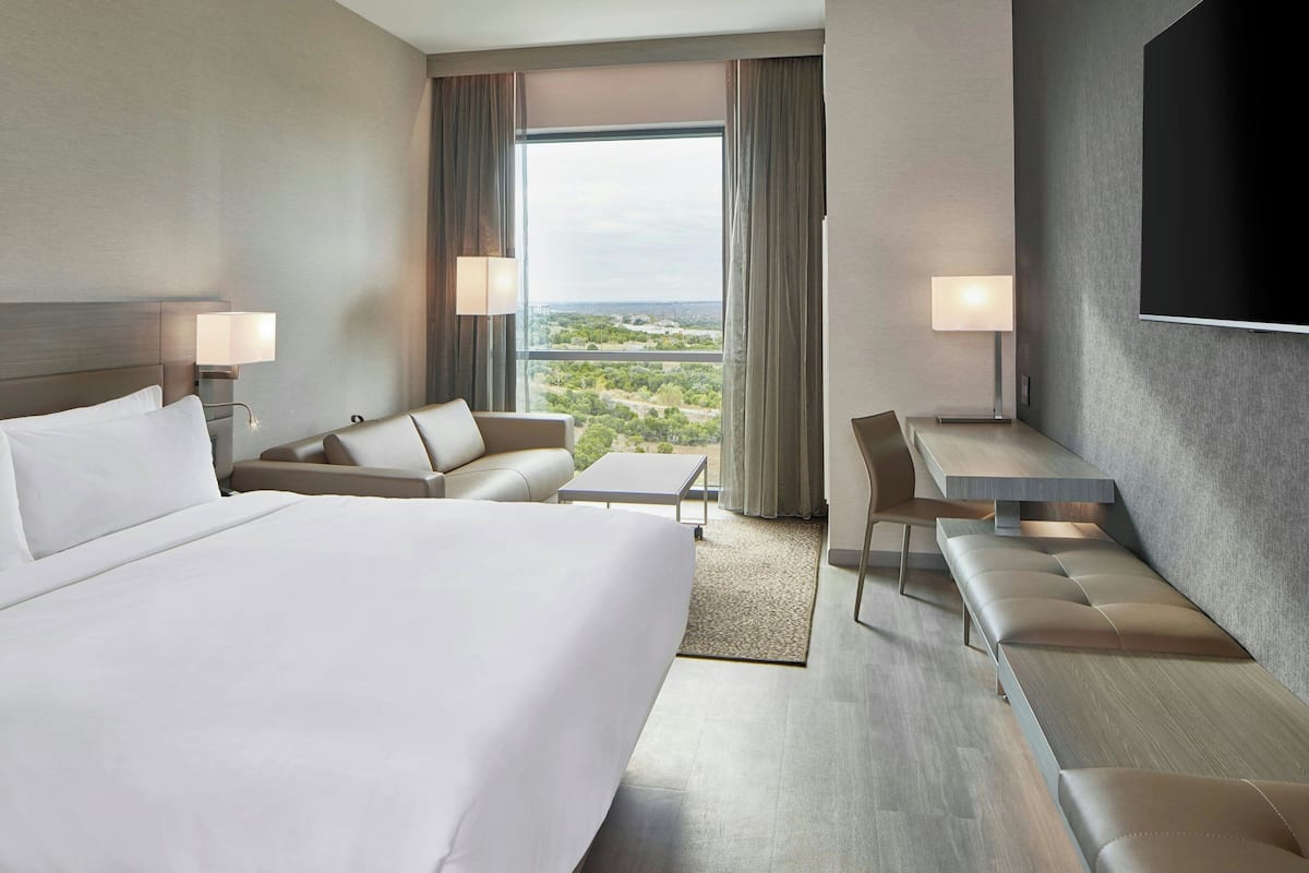 A hotel room with a large bed, a sofa, a desk, and a view of the city.