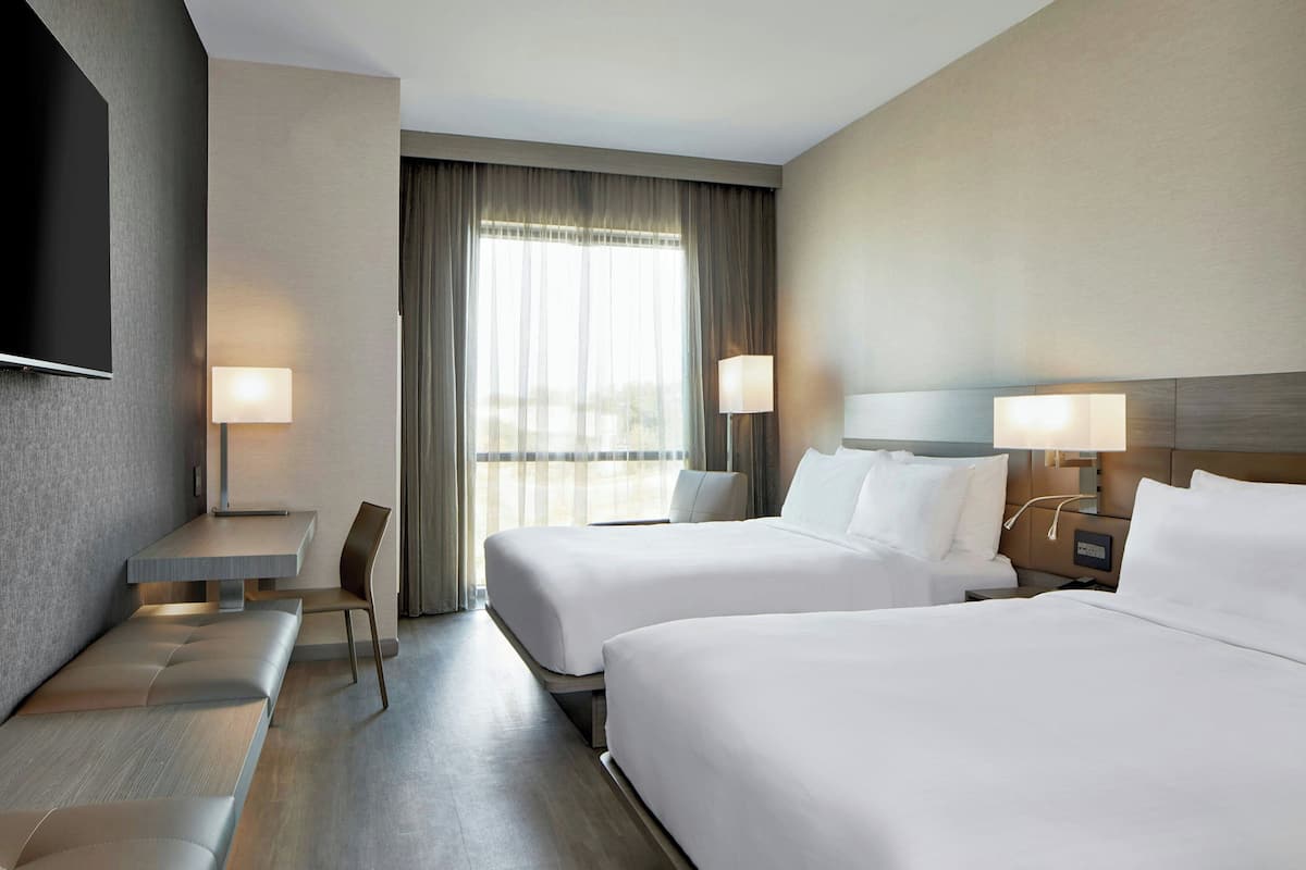 A hotel room with two beds, a desk, a chair, and a TV.