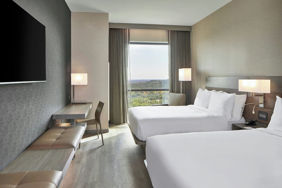 A hotel room with two beds, a desk, a chair, and a TV.