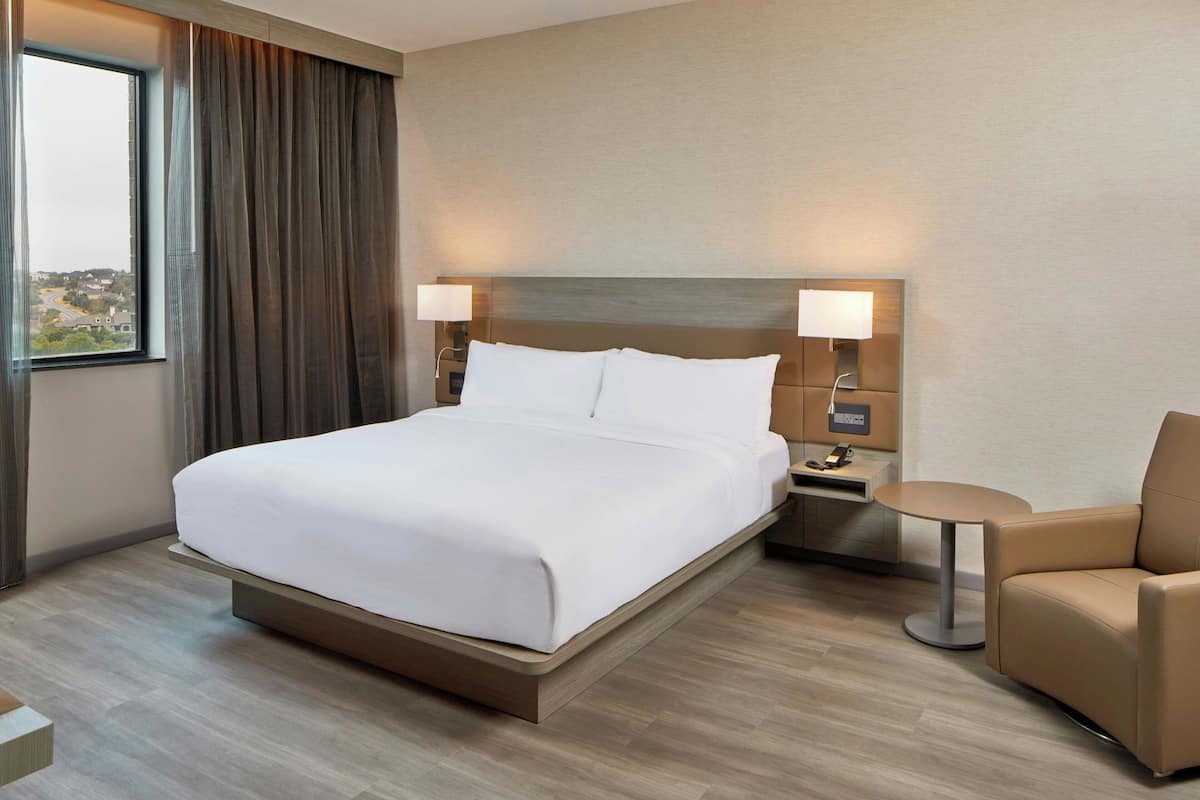 A modern hotel room with a large bed, bedside lamps, a small round table, and a chair.