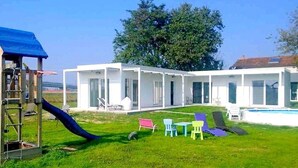 Ein modernes Haus mit überdachter Terrasse, Schwimmbad und Rutsche.