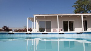 Ein Poolbereich mit überdachter Liege, Glastür und freiem Blick auf den Pool.