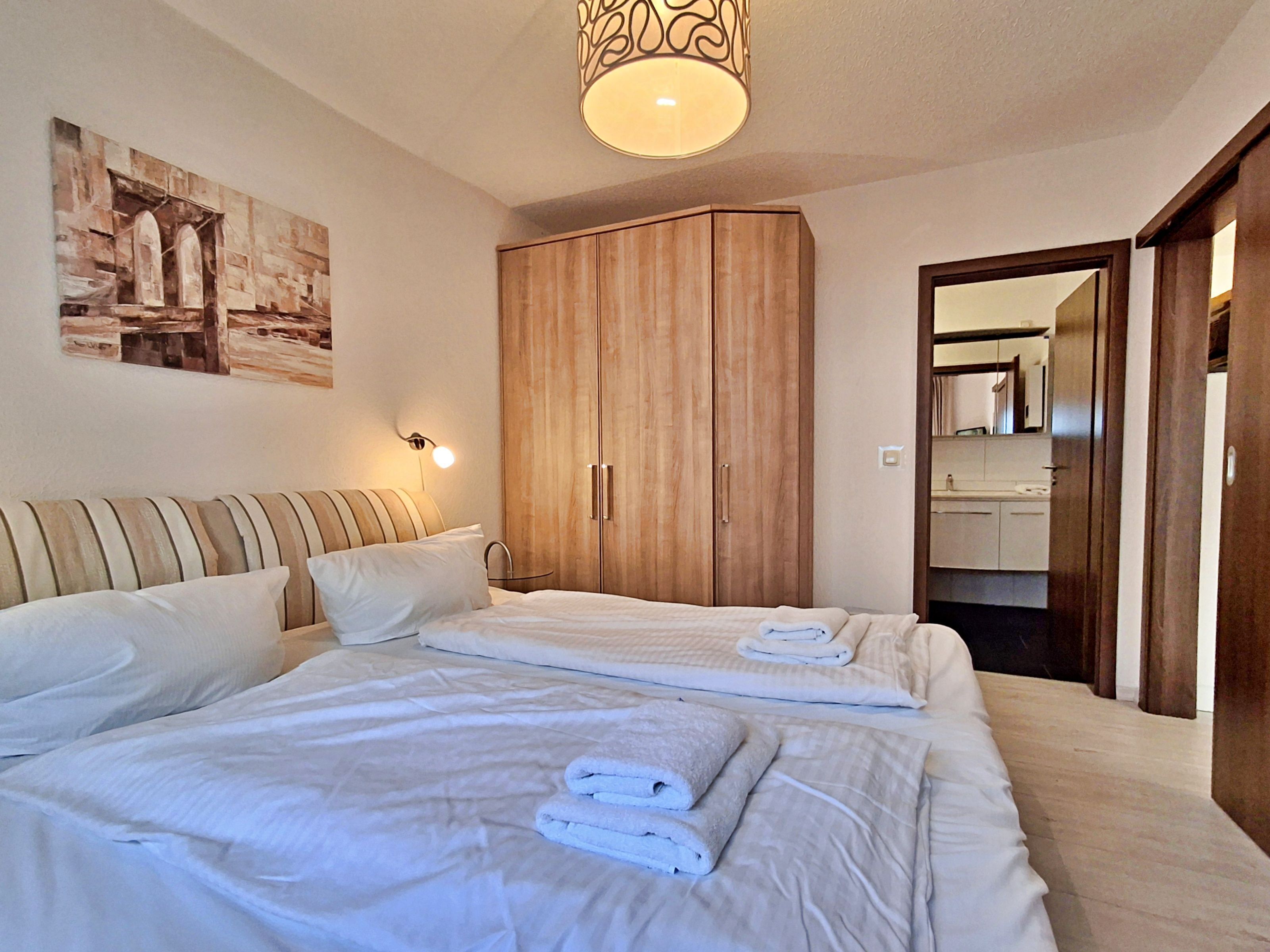 A hotel room with a large bed, a wooden wardrobe, and a bathroom visible through an open door.