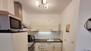 Cocina compacta con microondas, estufa y lavabo. Se observa una mesa con un plato y una silla.