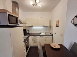 Une cuisine compacte équipée d’un four à micro-ondes, d’une cuisinière et d’un évier. On y trouve une table à manger avec une assiette et une chaise.