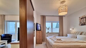 Habitación de hotel con cama, escritorio, silla, televisión y ventana con cortinas.