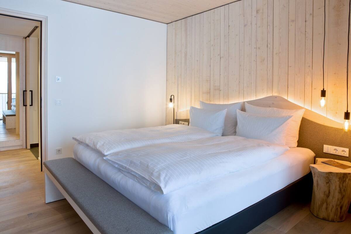 Une chambre à coucher moderne avec un grand lit, un mur recouvert de panneaux en bois, des lampes de chevet et un banc au pied du lit.