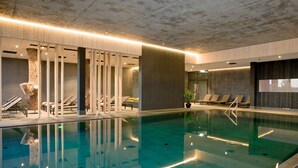 En modern inomhuspool med klart vatten, solstolar och en trädstam som fungerar som ett dekorativt mittstycke.