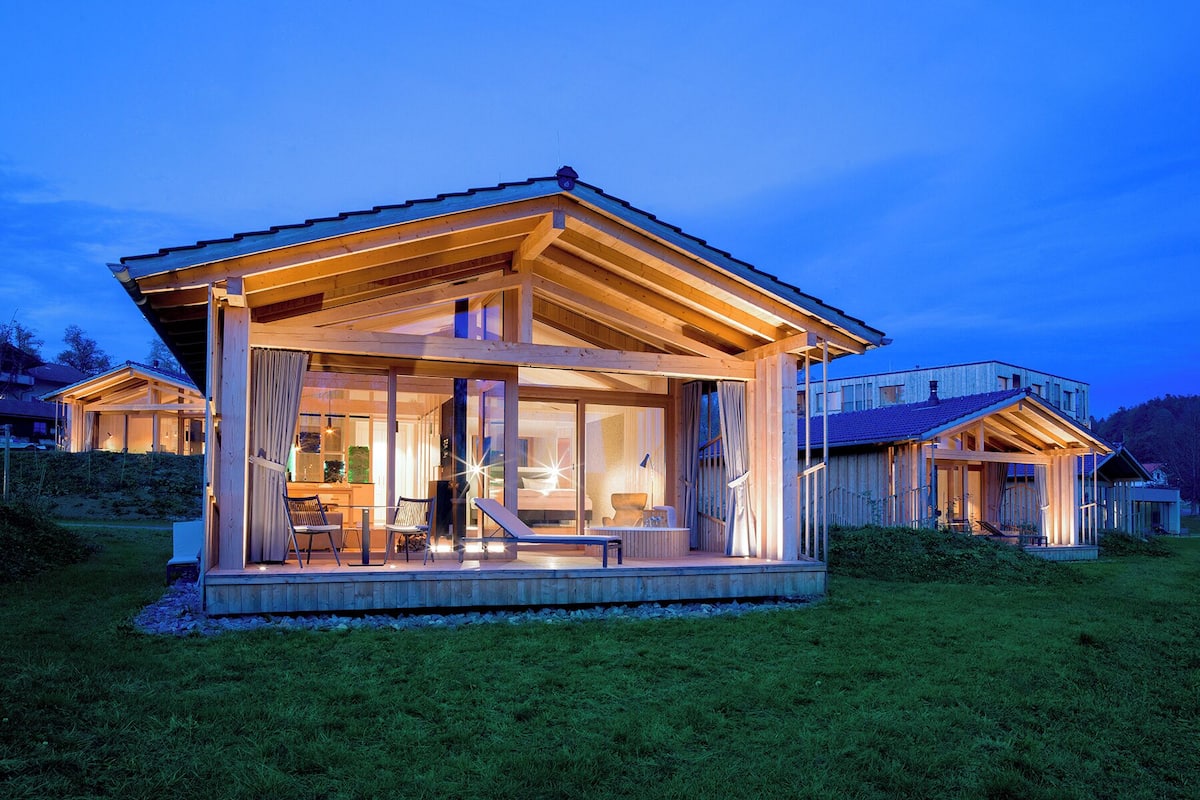 Une maison moderne en bois, dotée de grandes fenêtres et d’un porche abrité.