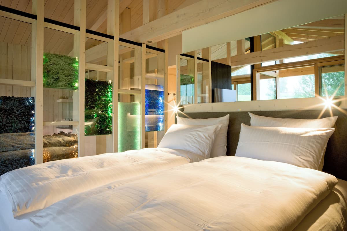 Une chambre avec un grand lit, des poutres apparentes en bois au plafond et une vue sur la verdure environnante.