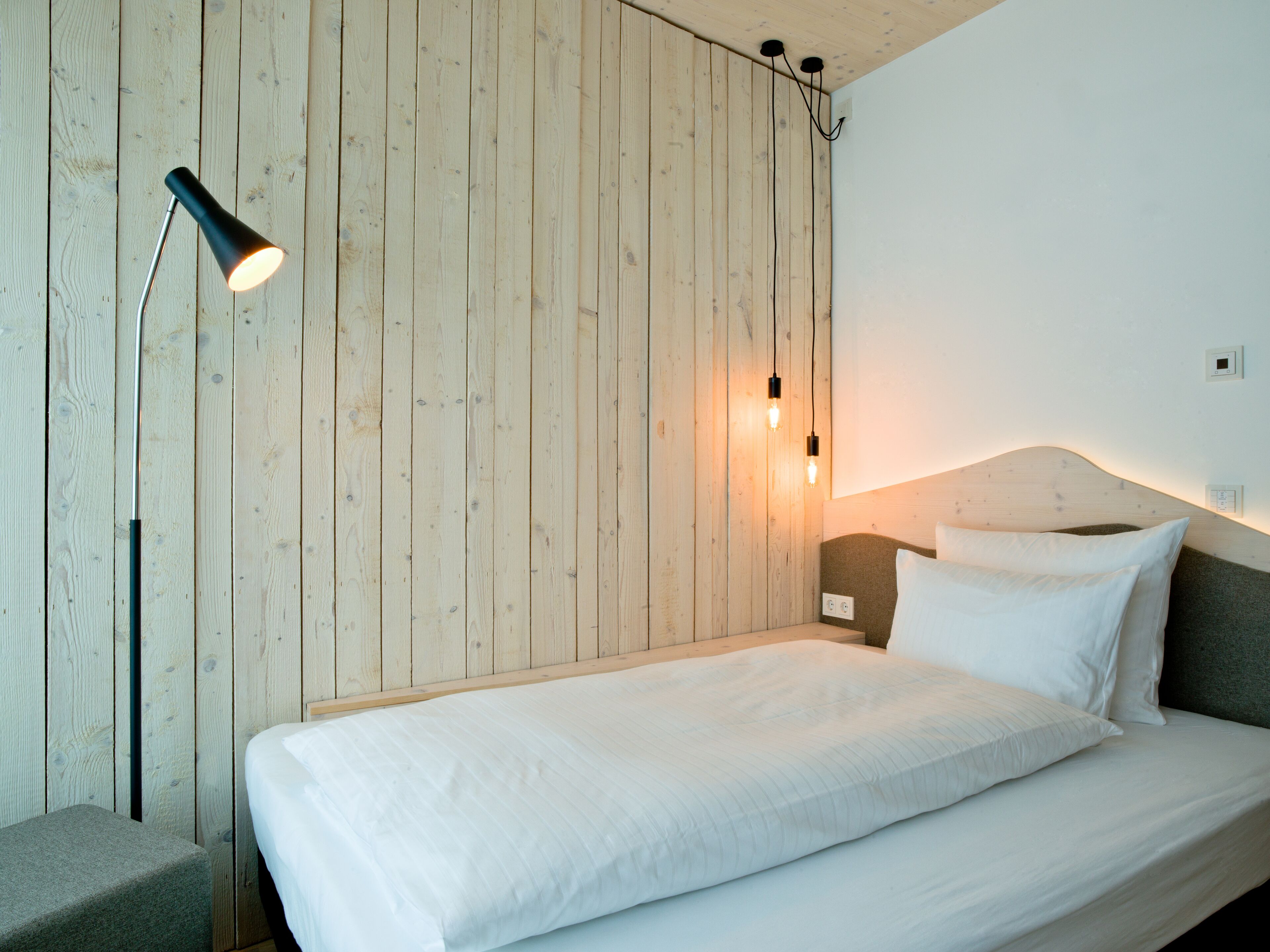 Un dormitorio minimalista con una pared de madera, una cama individual, una mesita de noche y una lámpara de pie.