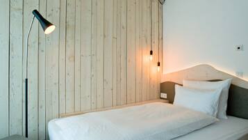 Un dormitorio minimalista con una pared de madera, una cama individual, una mesita de noche y una lámpara de pie.