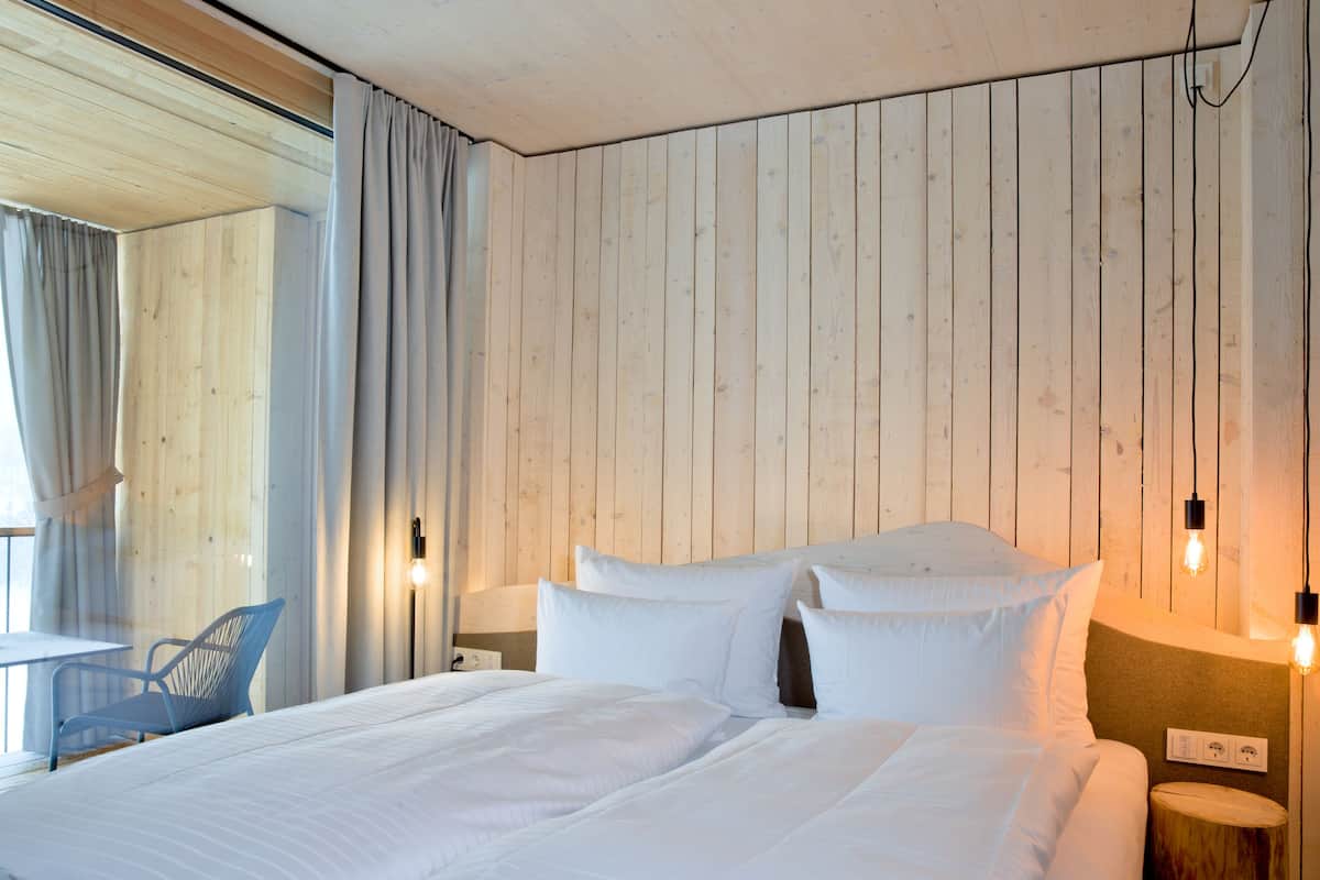 Une chambre d’hôtel avec un mur lambrissé en bois, un lit avec du linge de maison blanc, une chaise bleue et deux lampes de chevet.