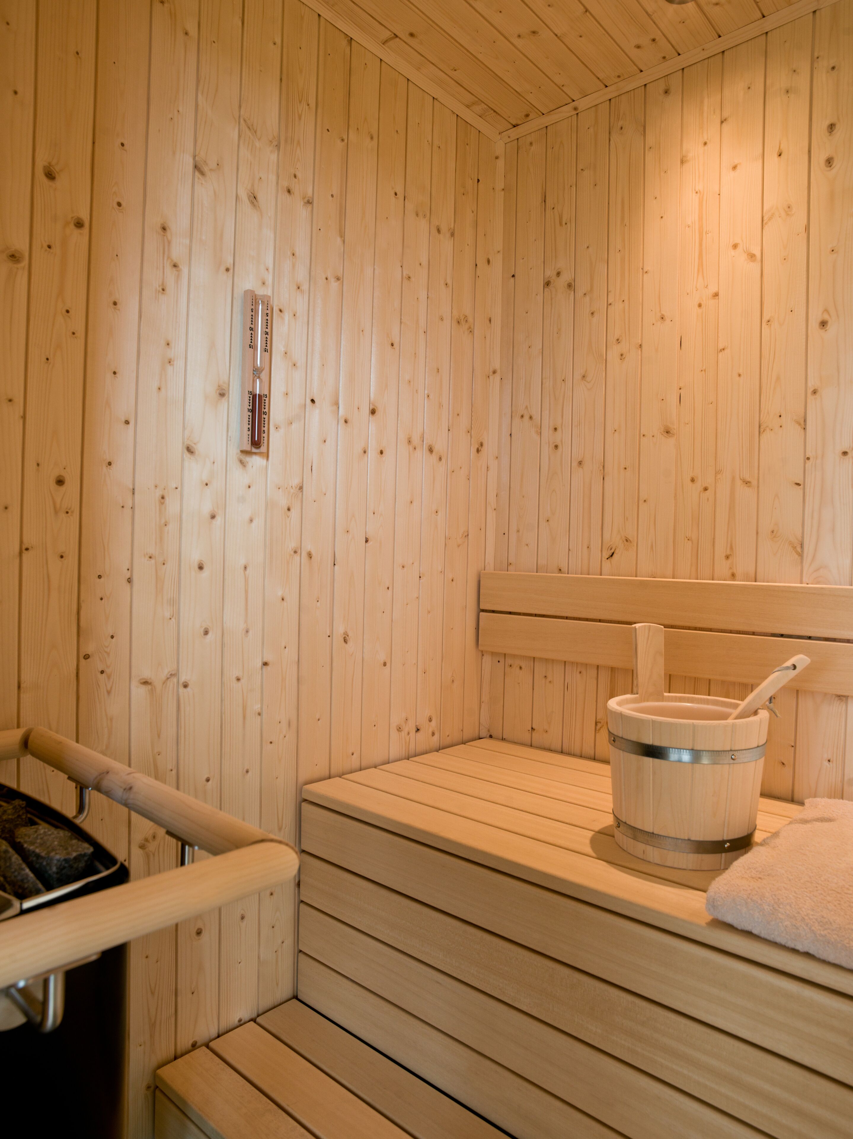 A wooden sauna with a bench, a wooden bucket, and a thermometer on the wall.