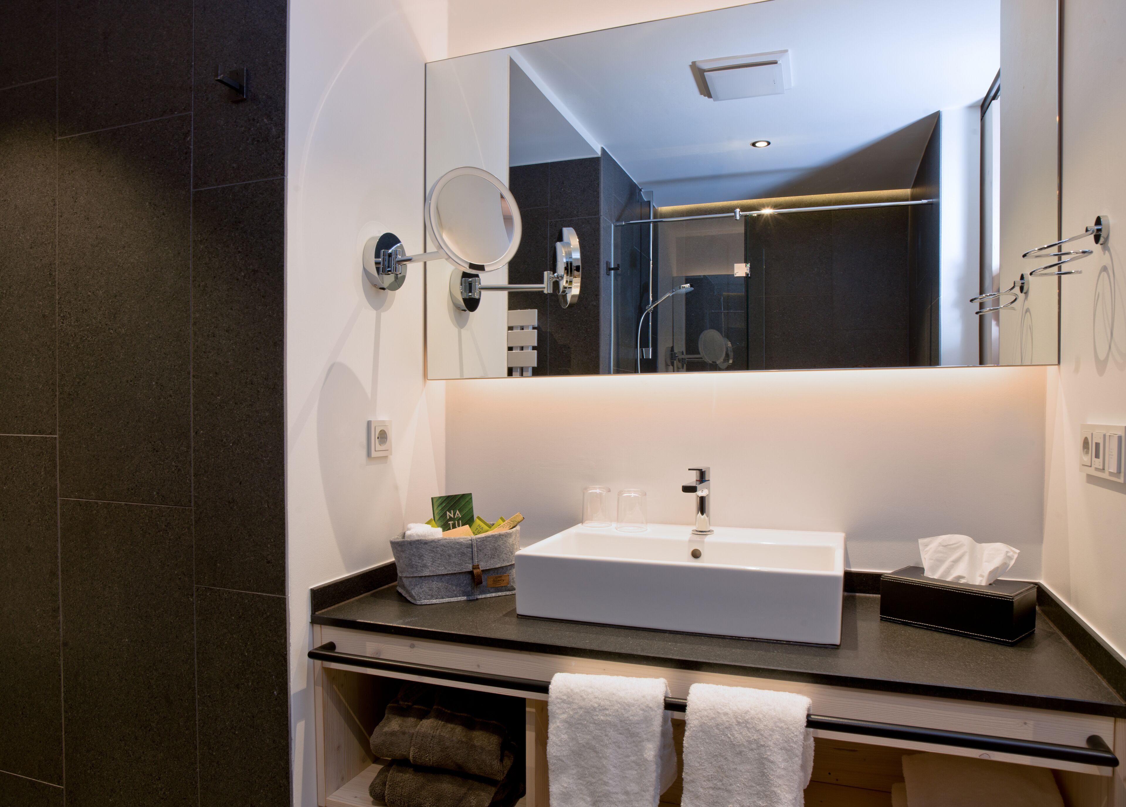 Une salle de bain moderne avec un grand miroir, un lavabo blanc et un porte-serviettes.