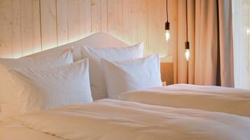 A double bed with white linens and two pillows, a wooden headboard, and two hanging light bulbs.