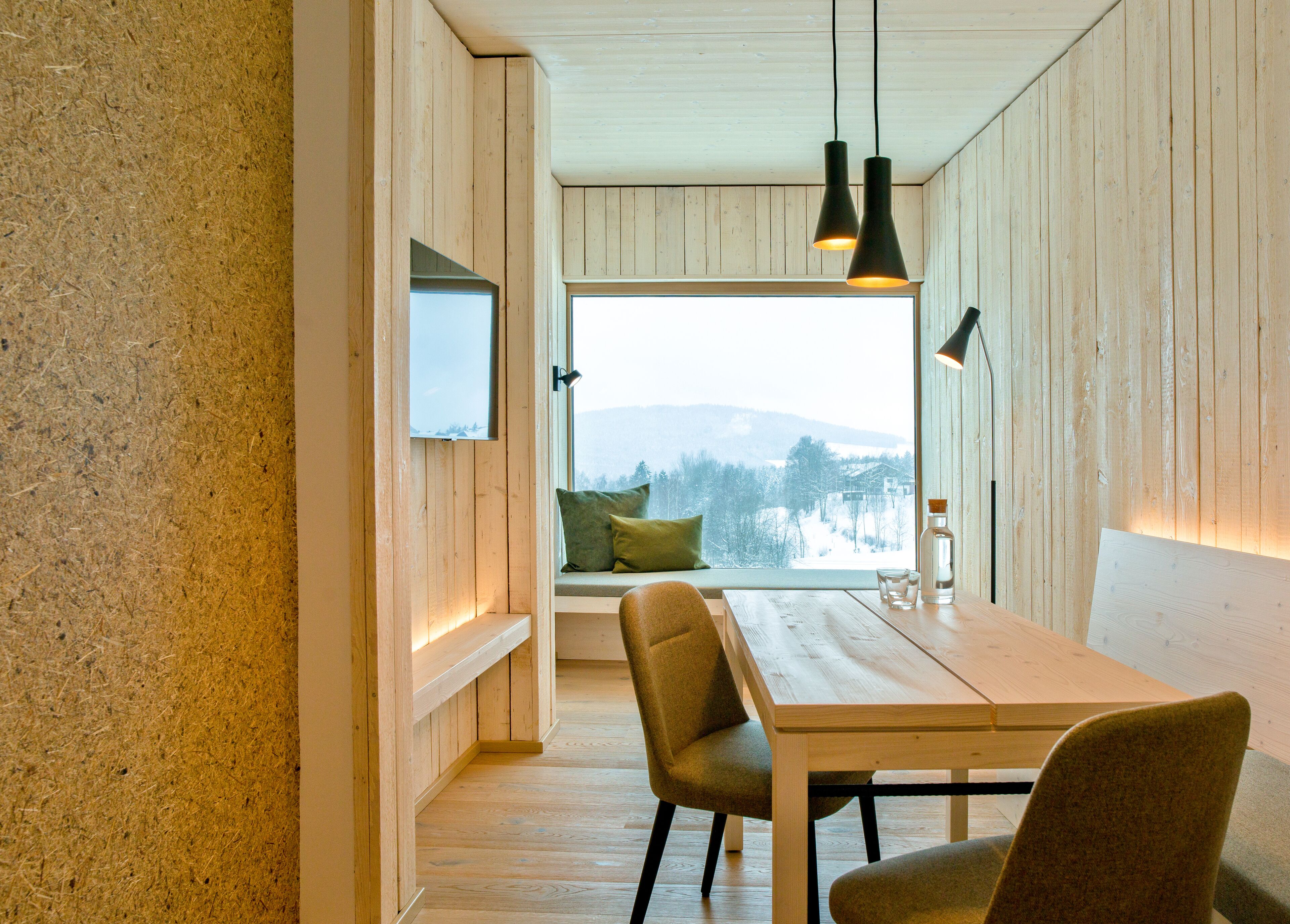 A dining area with a wooden table and chairs, a window with a view of snow-covered hills, and a bottle on the table.