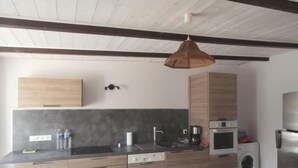 A modern kitchen with wooden cabinets, a built-in oven, a washing machine, and a dining area with a table and chairs.