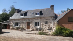 A stone house with a sloped roof, a front porch, and a gravel driveway.