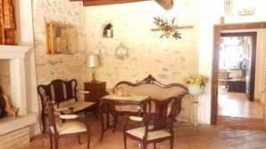 A dining area with a wooden table and chairs, a sofa, a lamp, and a wall with decorative elements. - AMAZING HISTORICAL COUNTRY HOUSE (Pozzolengo)
