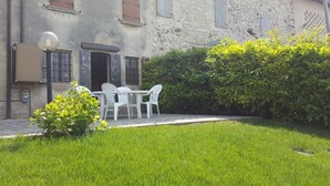 A stone building with a grassy yard, a small table with chairs, and a hedge. - AMAZING HISTORICAL COUNTRY HOUSE (Pozzolengo)