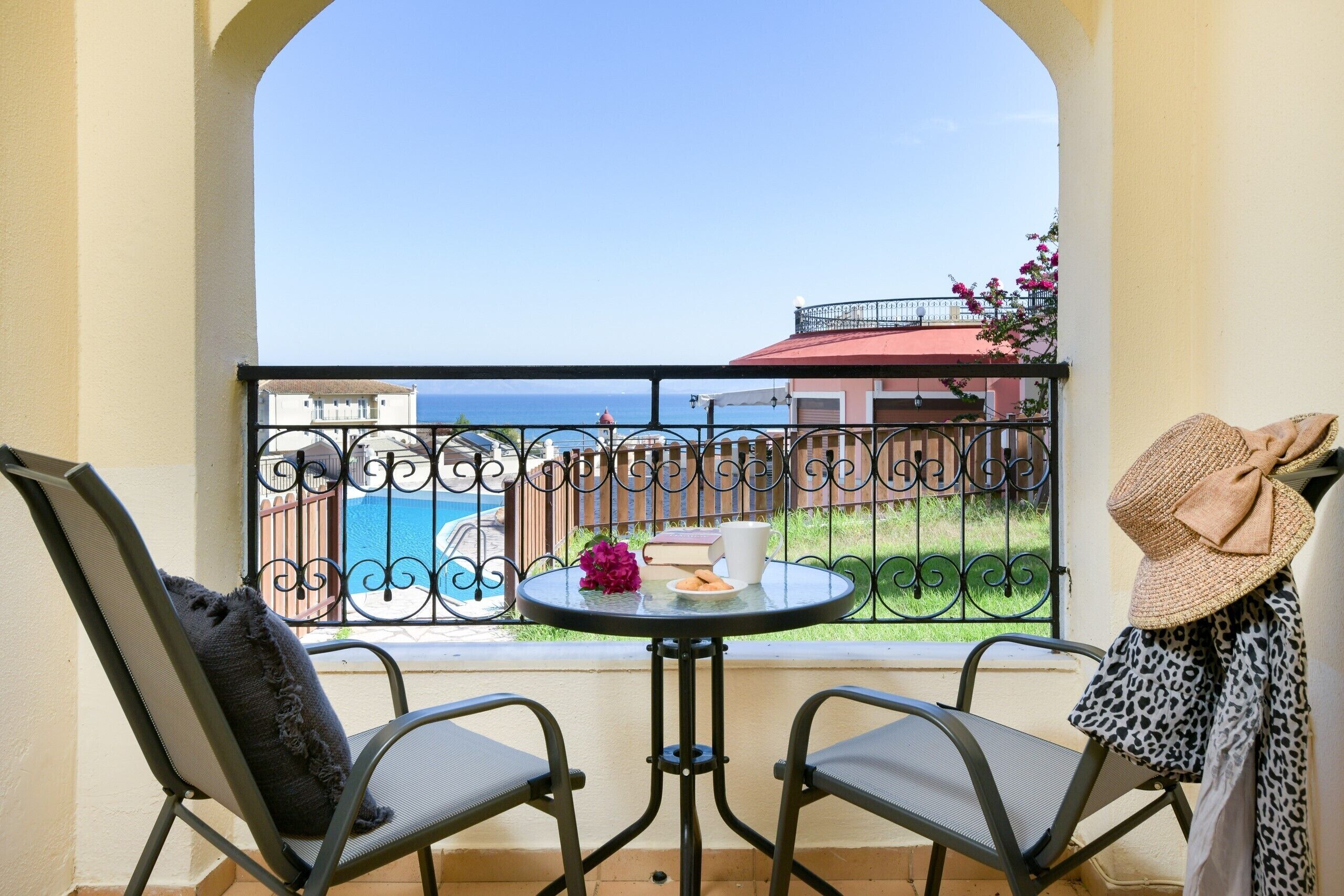 Ein Balkon mit Meerblick, zwei Stühle, ein kleiner runder Tisch mit einem Buch, einer Tasse und einer Blume.