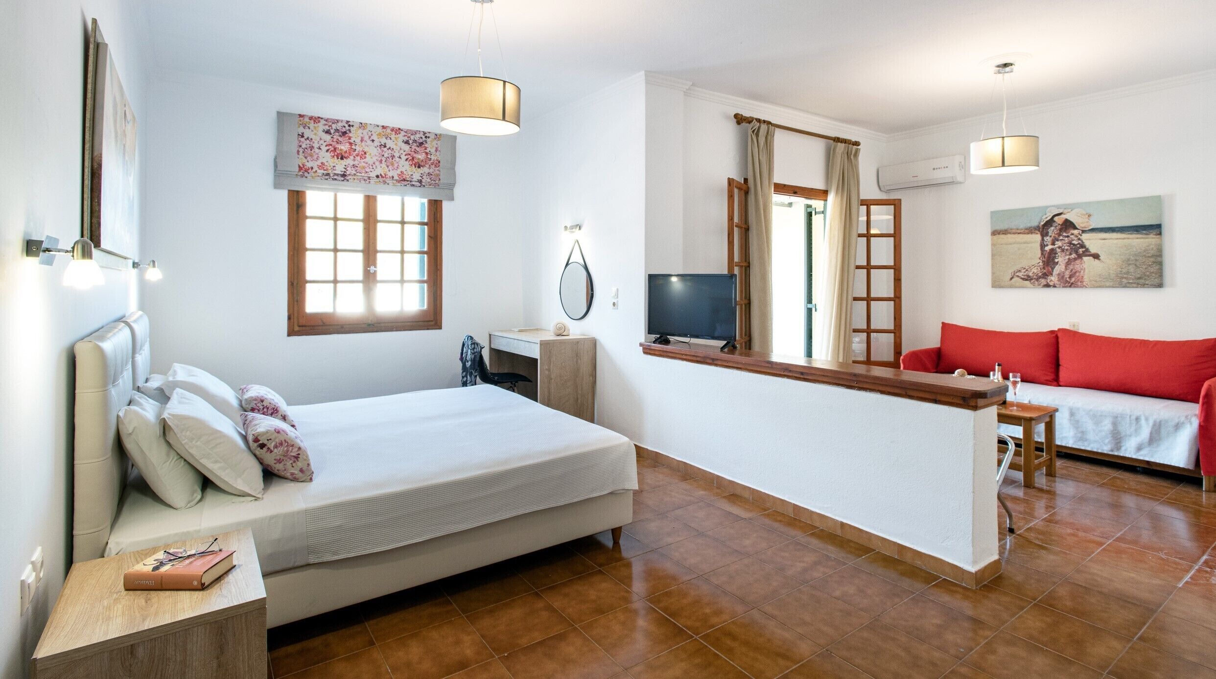 A bedroom with a bed, bedside table, and a desk with a chair. There is a window with curtains, a TV, and a painting on the wall.