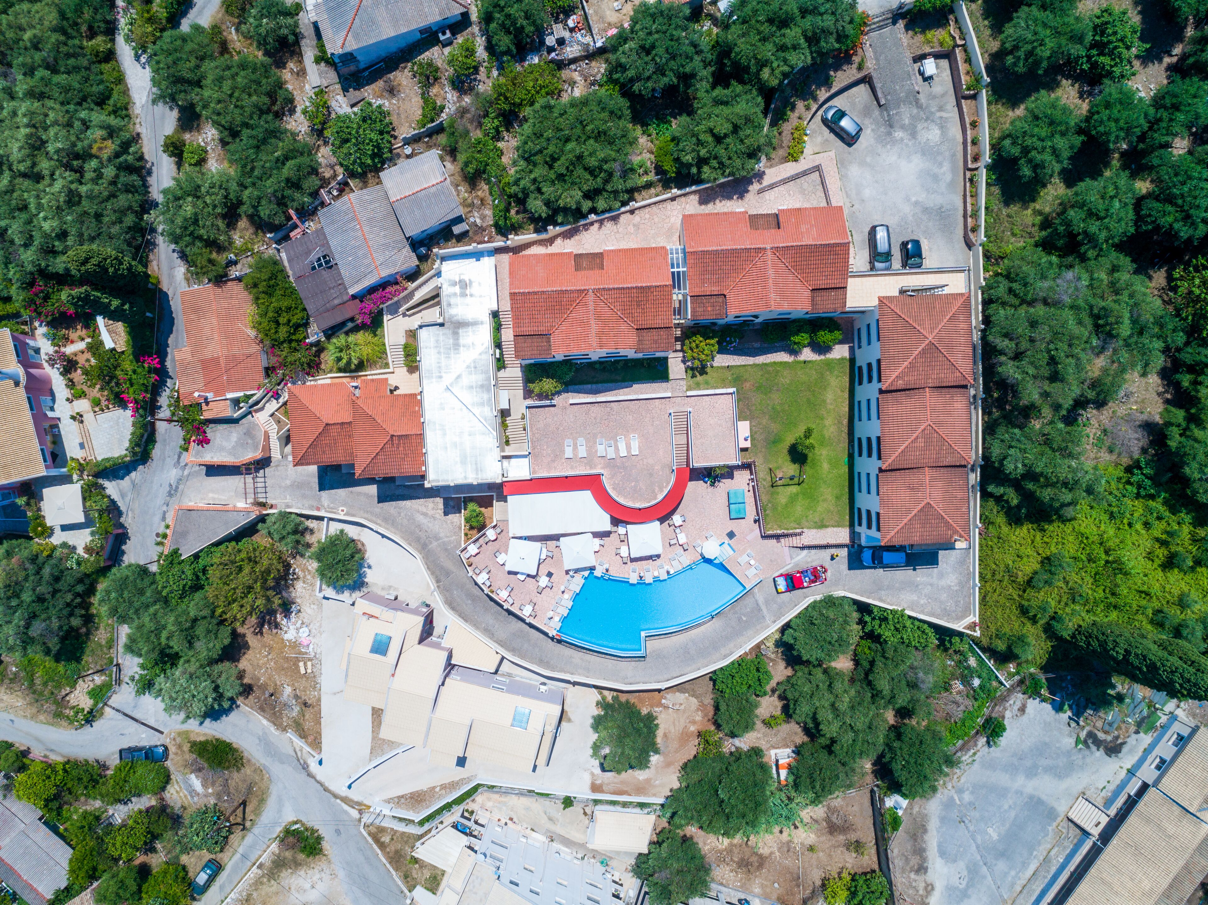 An aerial view of a residential area with a swimming pool, multiple buildings, and surrounding greenery.