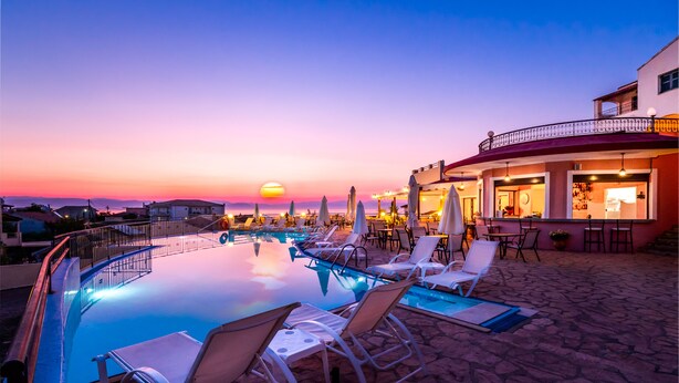 Un espace aménagé au bord de la piscine, avec des chaises longues et des parasols, un bar et une vue imprenable sur le coucher de soleil.