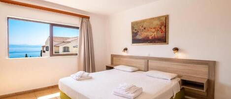 A hotel room with a large bed, a painting on the wall, and a view of the sea through a window.