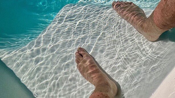 Gambe di persona in una piscina limpida con increspature e riflessi di luce solare.