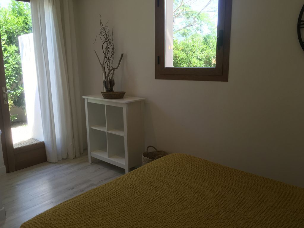 Ein Zimmer mit einem Bett, einem weißen Regal, einem Fenster mit Blick ins Grüne und einer Tür mit Vorhang.