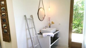 Un bagno con un lavandino bianco, uno specchio, una scala e una porta che dà su un giardino.