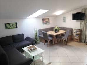 A living room with a sofa, a dining table with chairs, a TV mounted on the wall, and a small table with a basket. - Panoramic View Vacation Apartment - Panoramic View Vacation Apartment (Götzens)