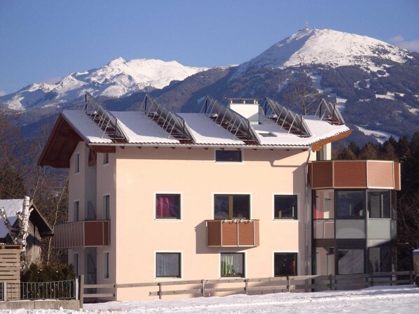 A multi-story building with a sloped roof, solar panels, and a view of snow-covered mountains.