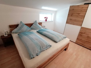 A bed with a wooden headboard, a bedside table with a lamp, a window with a view, and a wooden floor. - Panoramic View Vacation Apartment - Panoramic View Vacation Apartment (Götzens)