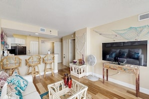 A living room with a sofa, chairs, a TV, and a kitchen in the background.