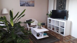 Ein Wohnzimmer mit einem weißen Sofa, einem Couchtisch, einem Fernseher auf einem Schrank und einem Bild an der Wand.
