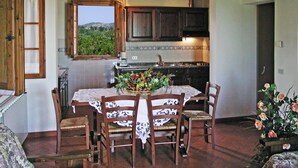 A dining area with a table set for four, surrounded by wooden chairs. A window provides a view of greenery outside.