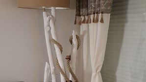 Una sala de estar con un sofá oscuro, un adorno blanco, un reposapiés color beige y una ventana con cortinas.